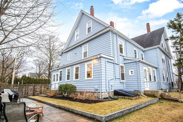 rear view of house with a patio area, fence, a lawn, and a chimney