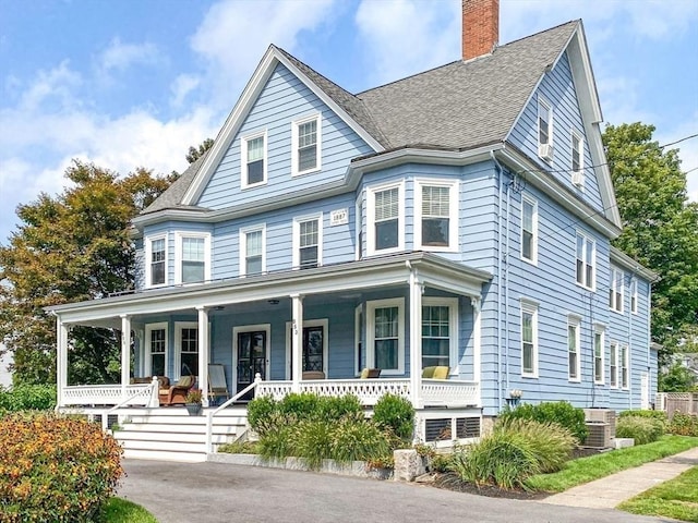 view of front of house with a shingled roof, a porch, and a chimney