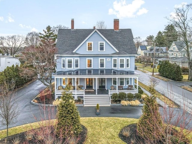 view of front of home featuring a porch, a shingled roof, a chimney, a front lawn, and aphalt driveway