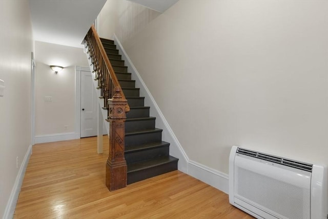 stairway with heating unit, baseboards, and wood finished floors