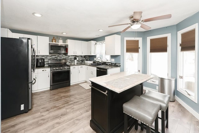 kitchen with appliances with stainless steel finishes, white cabinetry, sink, backsplash, and light wood-type flooring