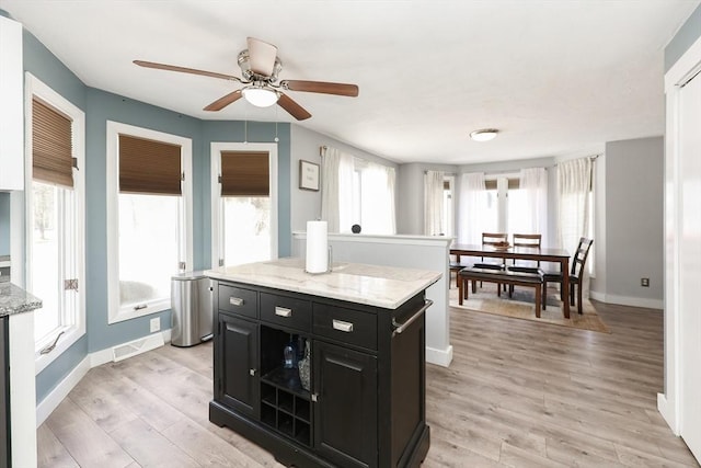 kitchen with ceiling fan, a kitchen island, light stone counters, and light hardwood / wood-style floors