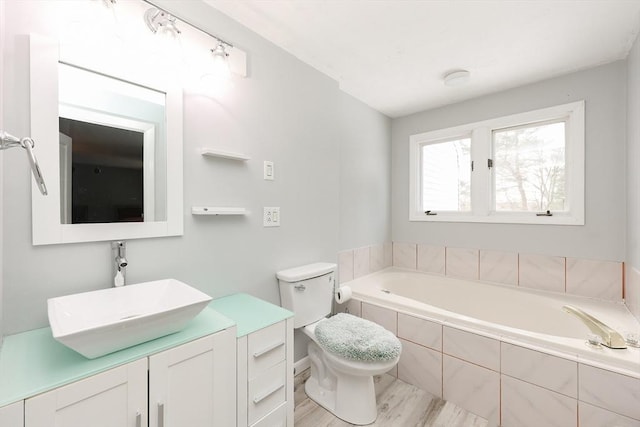 bathroom with a relaxing tiled tub, vanity, hardwood / wood-style flooring, and toilet