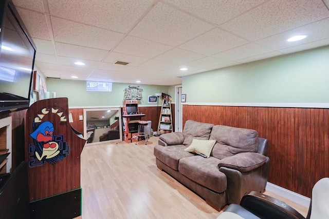 living room with hardwood / wood-style flooring, a drop ceiling, and wood walls