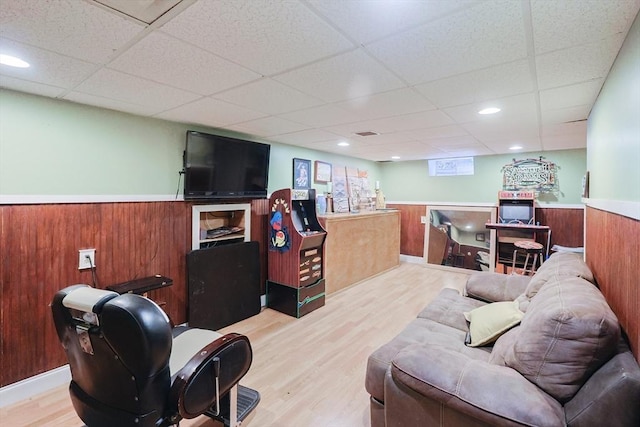 living room with wooden walls, a paneled ceiling, and light wood-type flooring