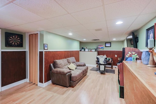 living room featuring wood-type flooring, a paneled ceiling, and wooden walls