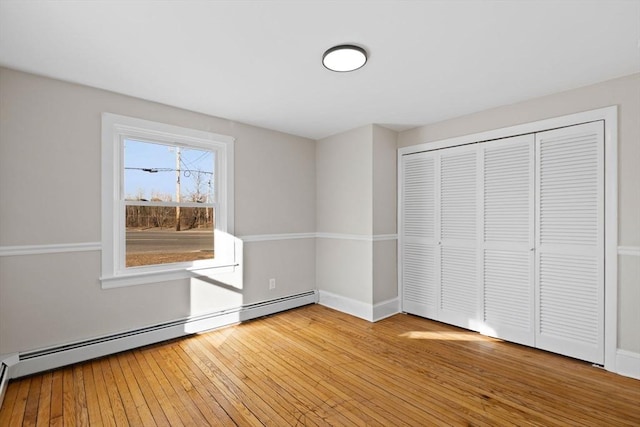 unfurnished bedroom featuring hardwood / wood-style floors, a closet, and a baseboard heating unit