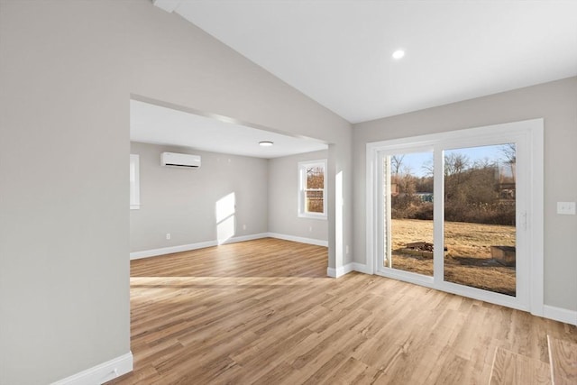 unfurnished room featuring vaulted ceiling, light hardwood / wood-style flooring, and an AC wall unit