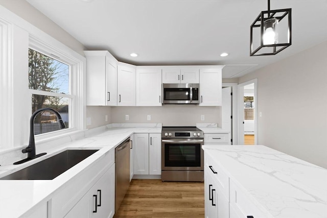 kitchen featuring pendant lighting, sink, white cabinets, stainless steel appliances, and light wood-type flooring