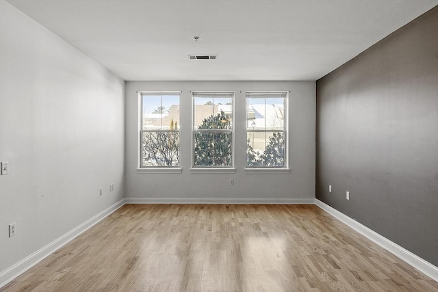 unfurnished room with light wood finished floors, visible vents, and baseboards