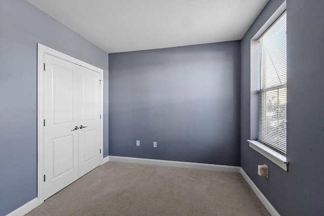 unfurnished bedroom featuring light carpet, a closet, and baseboards