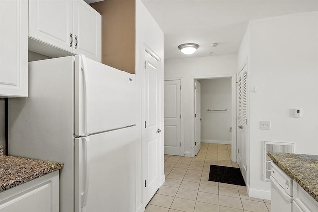 kitchen featuring light tile patterned floors, dark stone countertops, freestanding refrigerator, and white cabinetry