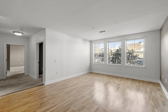 empty room with visible vents, light wood-style flooring, and baseboards