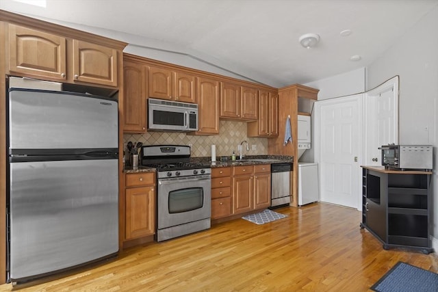 kitchen with stainless steel appliances, estacked washer and dryer, lofted ceiling, light wood finished floors, and tasteful backsplash