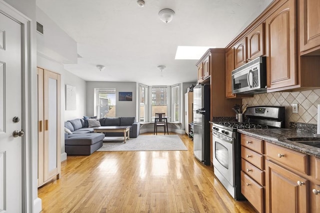 kitchen with appliances with stainless steel finishes, a skylight, tasteful backsplash, light wood-style floors, and brown cabinets
