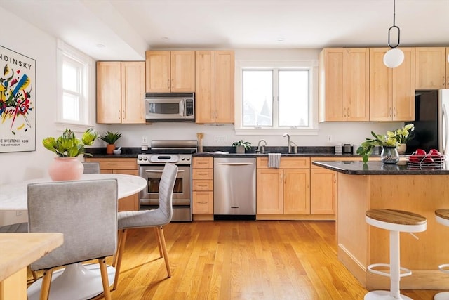 kitchen with a breakfast bar area, light brown cabinets, light wood-style flooring, stainless steel appliances, and dark countertops