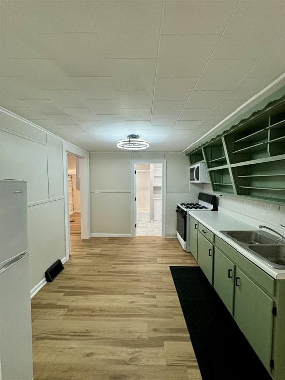 kitchen with sink, green cabinets, white appliances, and light hardwood / wood-style flooring