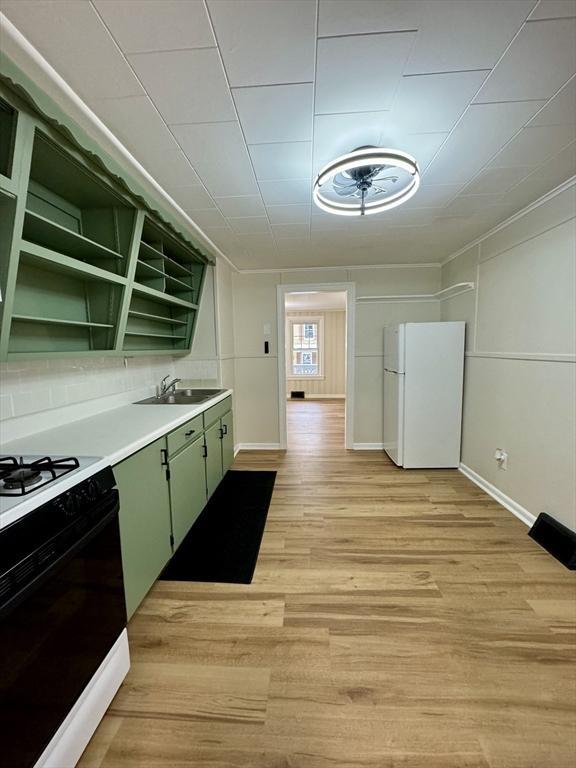 kitchen with range with gas stovetop, sink, white refrigerator, green cabinetry, and light wood-type flooring