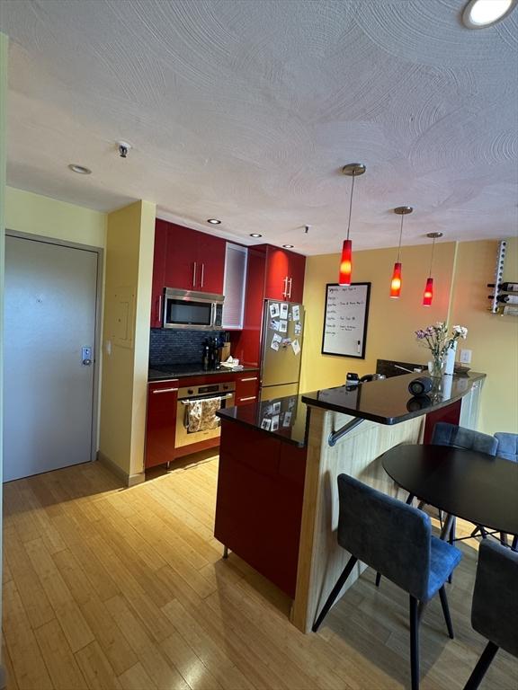 133 Commander Shea Blvd Unit 614, Quincy, MA 02171 - kitchen featuring appliances with stainless steel finishes, red cabinetry, dark countertops, decorative backsplash, and light wood-style floors