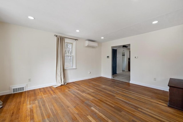 empty room with a wall unit AC, hardwood / wood-style flooring, baseboards, and visible vents