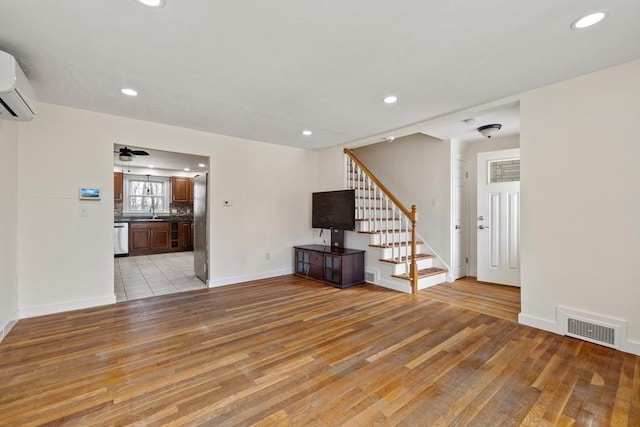 unfurnished living room featuring light wood-style floors, visible vents, stairway, and a wall mounted AC