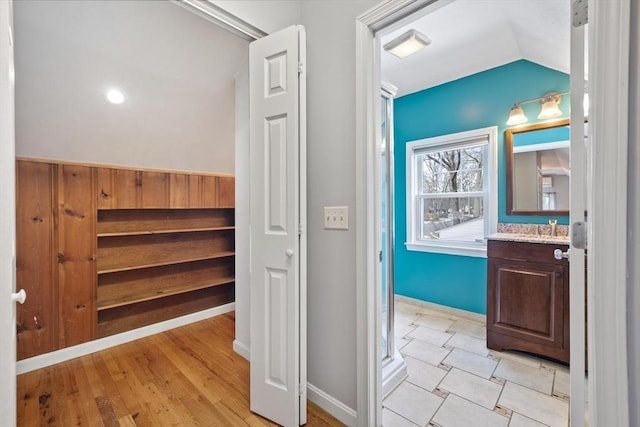 hall with lofted ceiling, light wood-type flooring, a sink, and baseboards