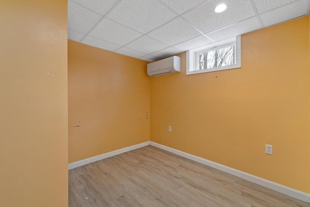 below grade area with a drop ceiling, a wall unit AC, wood finished floors, and baseboards