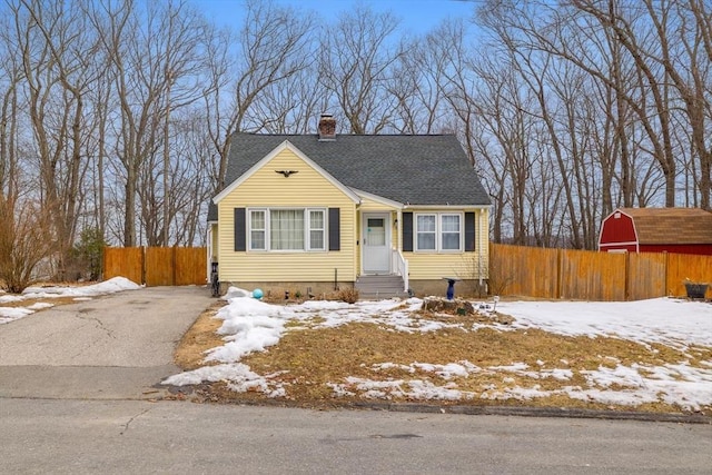 view of front facade featuring driveway, a chimney, roof with shingles, fence, and an outdoor structure