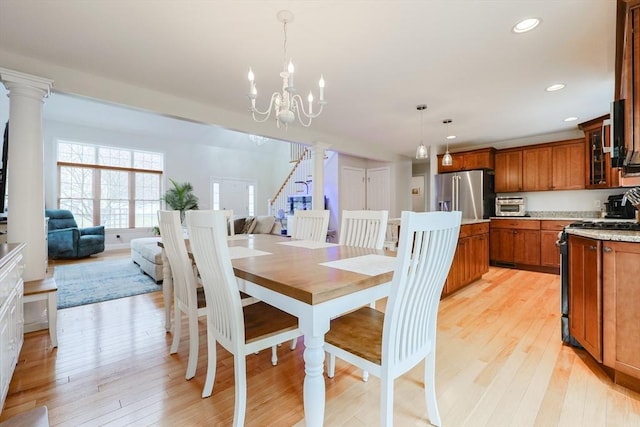 dining space with decorative columns, an inviting chandelier, and light wood-style flooring