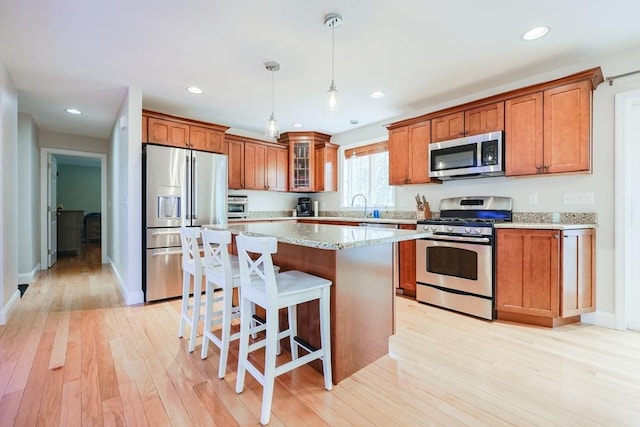 kitchen featuring appliances with stainless steel finishes, a kitchen island, brown cabinets, a kitchen bar, and light wood-type flooring