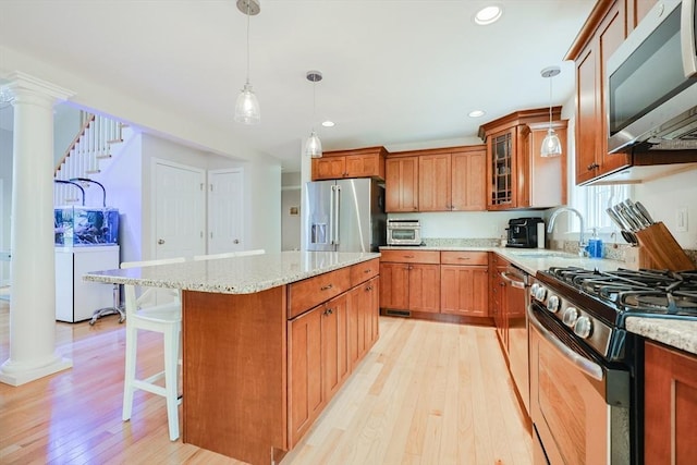 kitchen with light wood finished floors, a sink, decorative columns, brown cabinetry, and appliances with stainless steel finishes