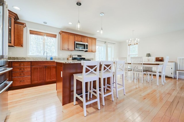 kitchen with appliances with stainless steel finishes, a wealth of natural light, brown cabinets, and light wood-type flooring