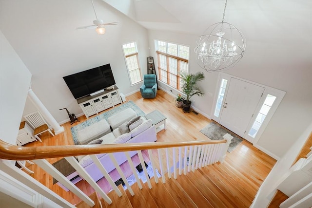 living room featuring a towering ceiling, wood finished floors, baseboards, and ceiling fan with notable chandelier