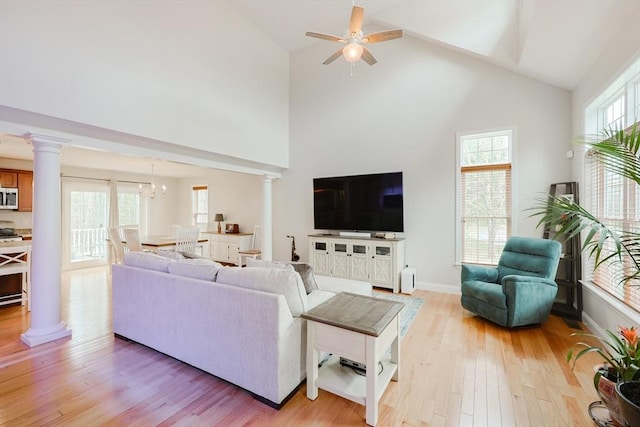 living room featuring ceiling fan with notable chandelier, decorative columns, light wood-type flooring, and high vaulted ceiling