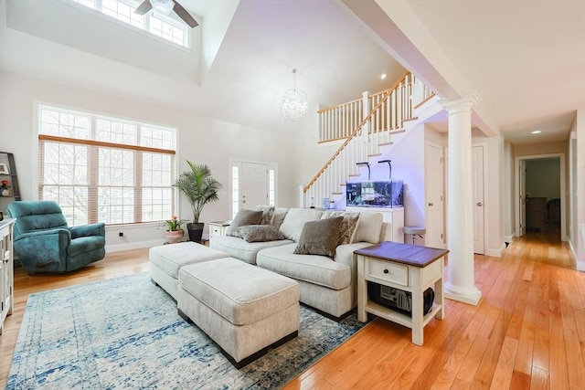 living area with ornate columns, light wood-style floors, stairway, and high vaulted ceiling