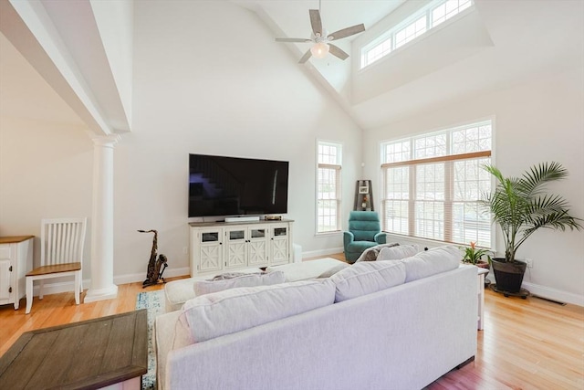 living area with ornate columns, ceiling fan, wood finished floors, and a high ceiling