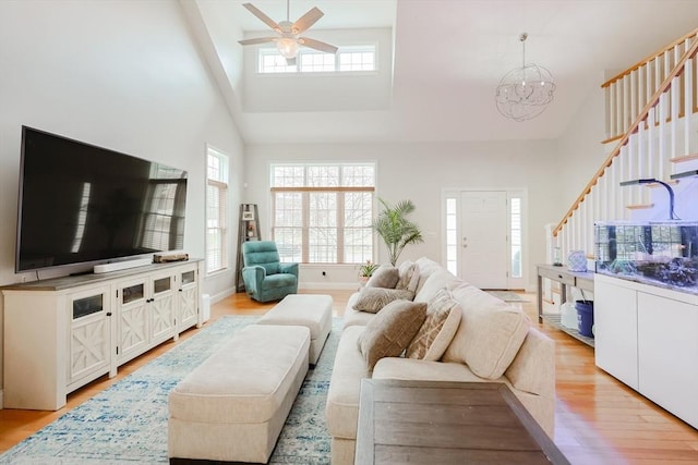 living room featuring a wealth of natural light, high vaulted ceiling, ceiling fan with notable chandelier, and stairs