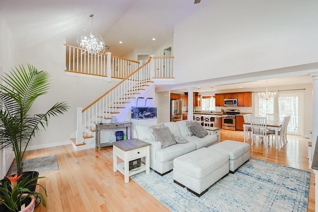 living room featuring an inviting chandelier, stairway, light wood-style floors, and high vaulted ceiling
