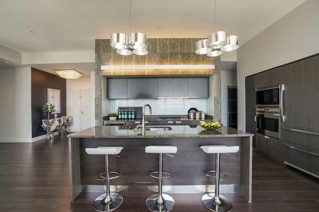 kitchen with dark stone countertops, sink, stainless steel oven, decorative backsplash, and dark wood-type flooring