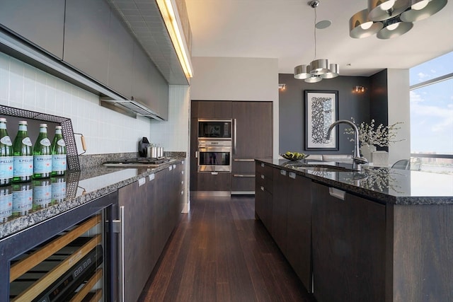 kitchen featuring dark wood-type flooring, sink, black appliances, beverage cooler, and a center island with sink