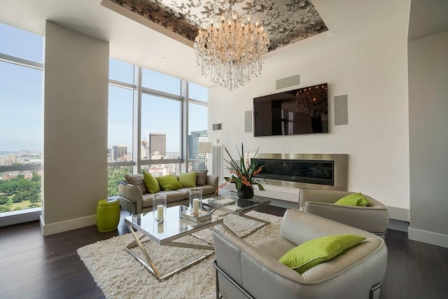 living room with dark wood-type flooring, a chandelier, expansive windows, and a raised ceiling