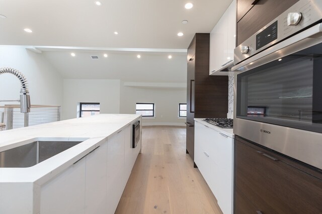 kitchen featuring sink, light hardwood / wood-style flooring, light stone counters, and white cabinetry