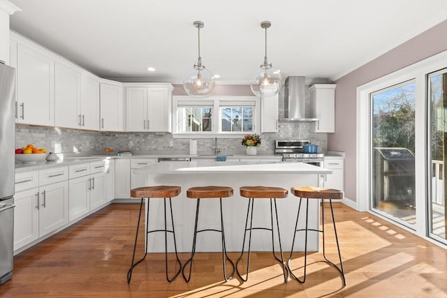 kitchen with a breakfast bar area, stainless steel appliances, white cabinets, light countertops, and wall chimney exhaust hood