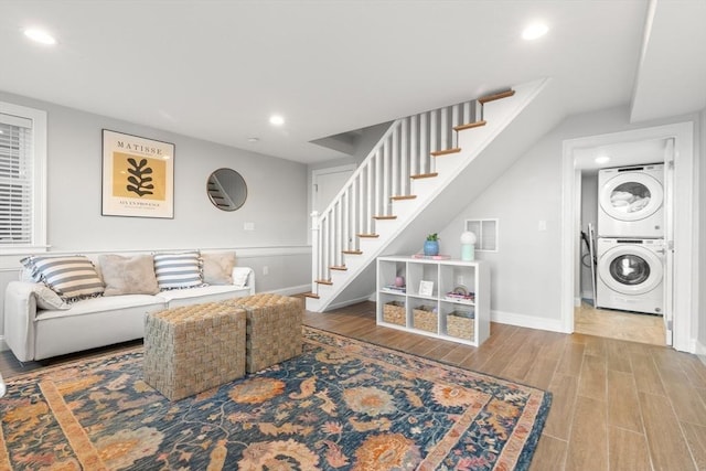 living room featuring baseboards, stacked washer and clothes dryer, wood finished floors, stairs, and recessed lighting