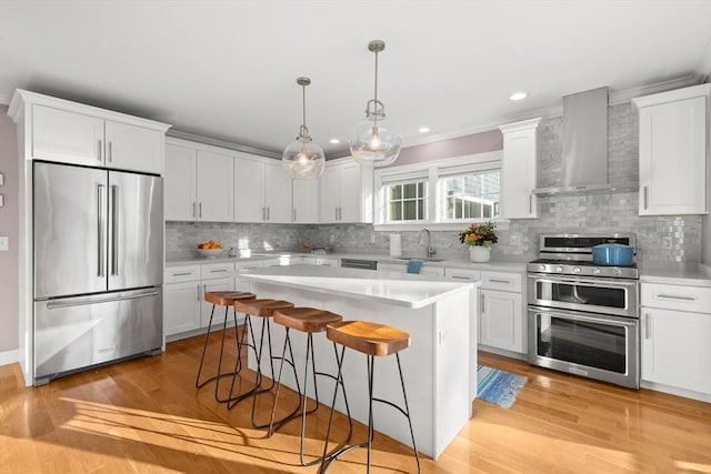 kitchen featuring a breakfast bar area, stainless steel appliances, light countertops, a sink, and wall chimney exhaust hood