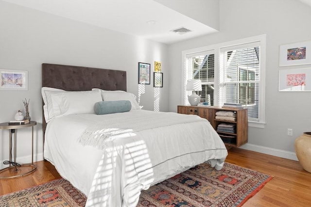 bedroom with wood finished floors, visible vents, and baseboards