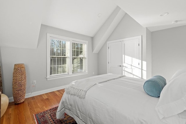 bedroom featuring lofted ceiling, a closet, wood finished floors, and baseboards