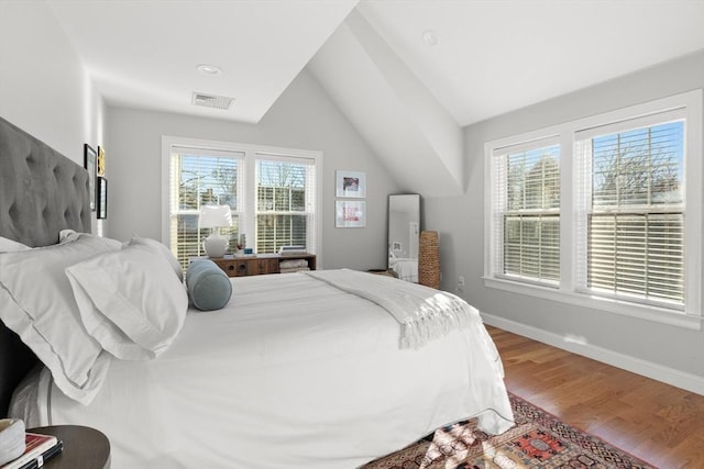 bedroom featuring baseboards, visible vents, vaulted ceiling, and wood finished floors