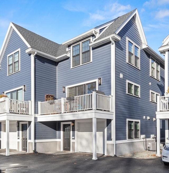 rear view of property featuring a garage, roof with shingles, and central air condition unit