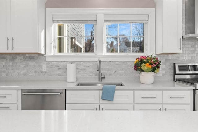 kitchen featuring stainless steel appliances, wall chimney range hood, a sink, and light countertops